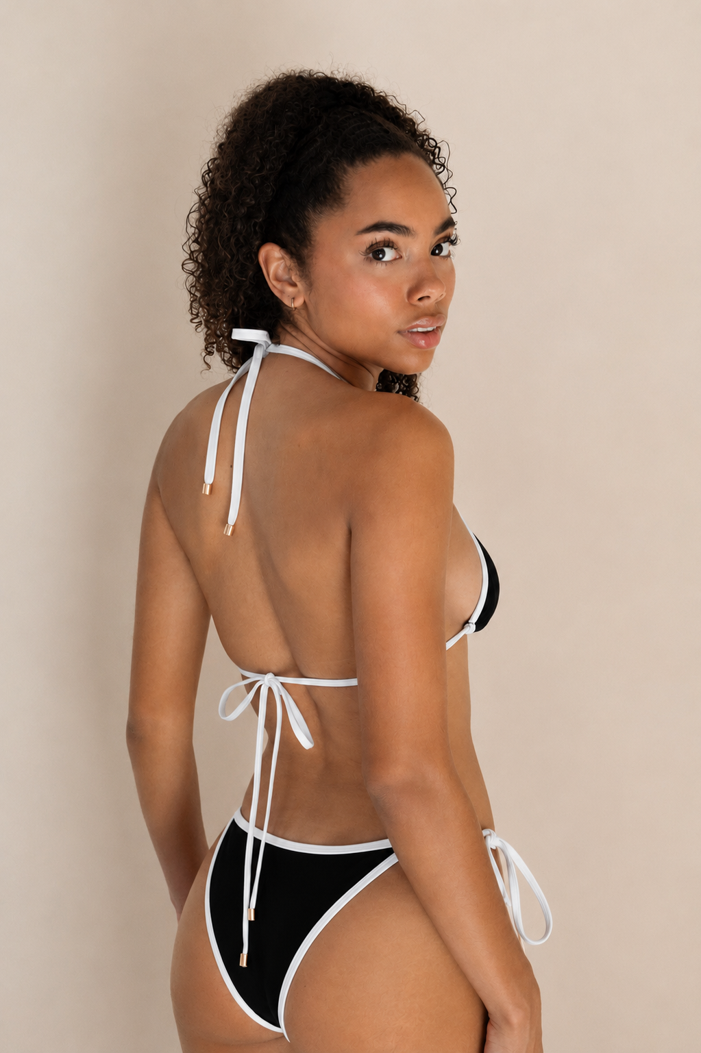 A woman modeling a black and white bikini and tie-back straps, shown from the back.